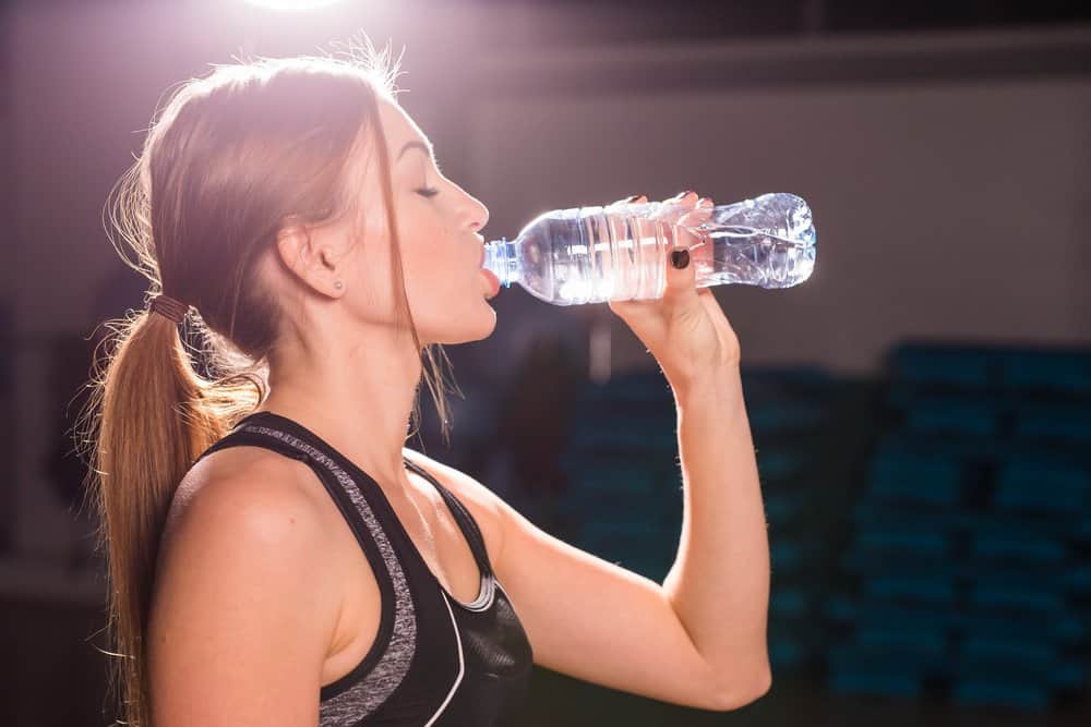 Fit young woman drinking water in the gym. Muscular woman taking break after exercise. - The Metabolic Reset Diet Plan