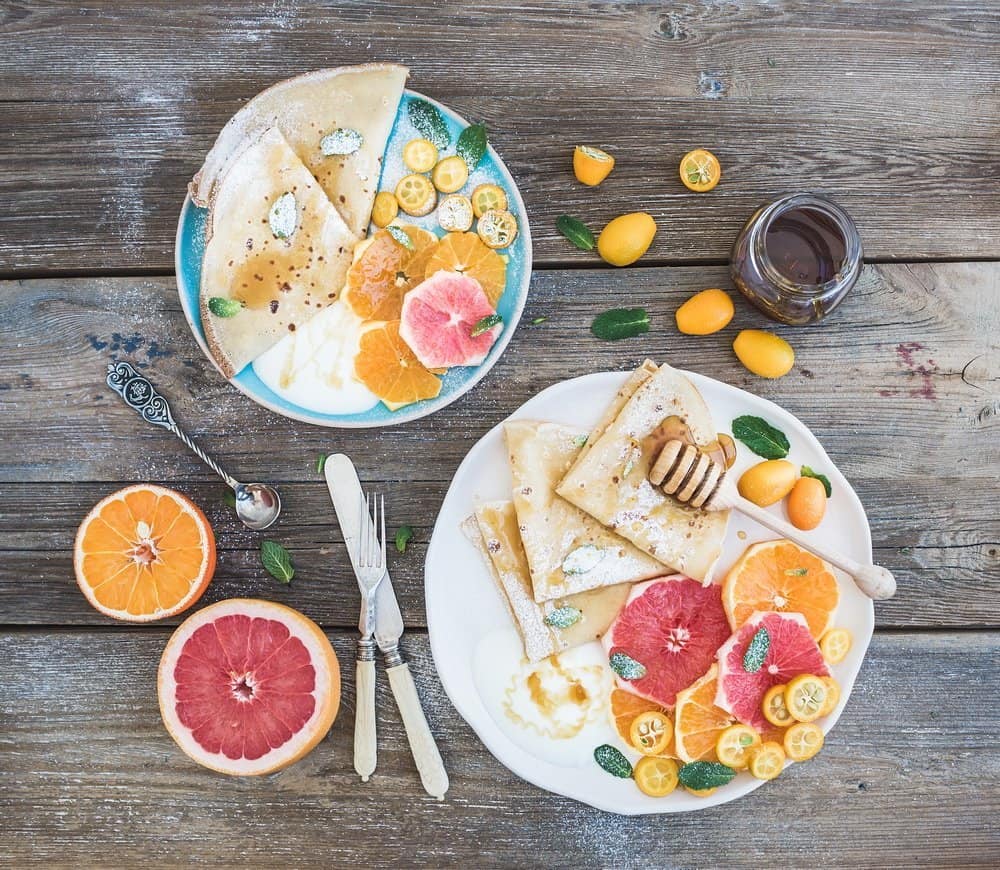 Spring vitamin breakfast set. Thin crepes or pancakes with fresh grapefruit, orange, kumquat, honey, cream and mint leaves over a rustic wood background