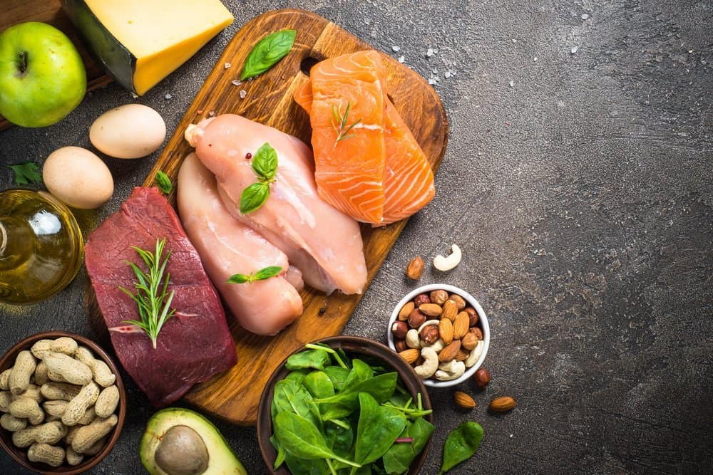 Ketogenic low carbs diet. Meat, fish, nuts, oil, cheese, milk and avocado on dark stone background. Top view with copy space. - Side Effects from Keto Diet