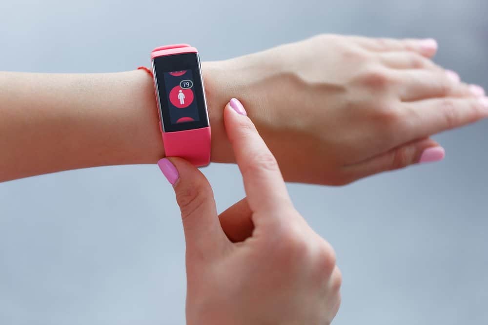 Isolated female hand with pink smartwatch taking pulse after exercising indoor on a light and blured background - Top 10 Fitness Trends of 2019