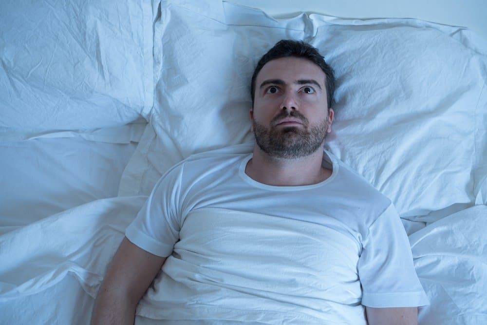 Stressed man trying to sleep in his bed at night - Signs You're Overdoing Cardio