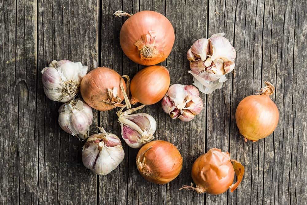 Fresh onion and garlic bulbs on old wooden table. - The Metabolic Reset Diet Plan