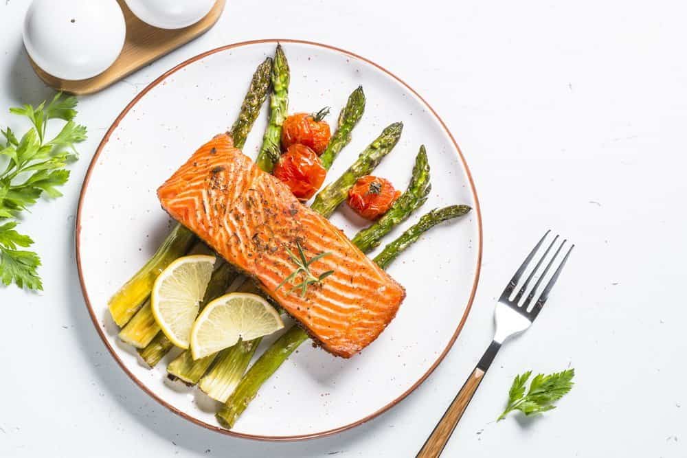Grilled salmon fish fillet with asparagus and tomato on white craft plate. Top view on white stone table. - Side Effects from Keto Diet