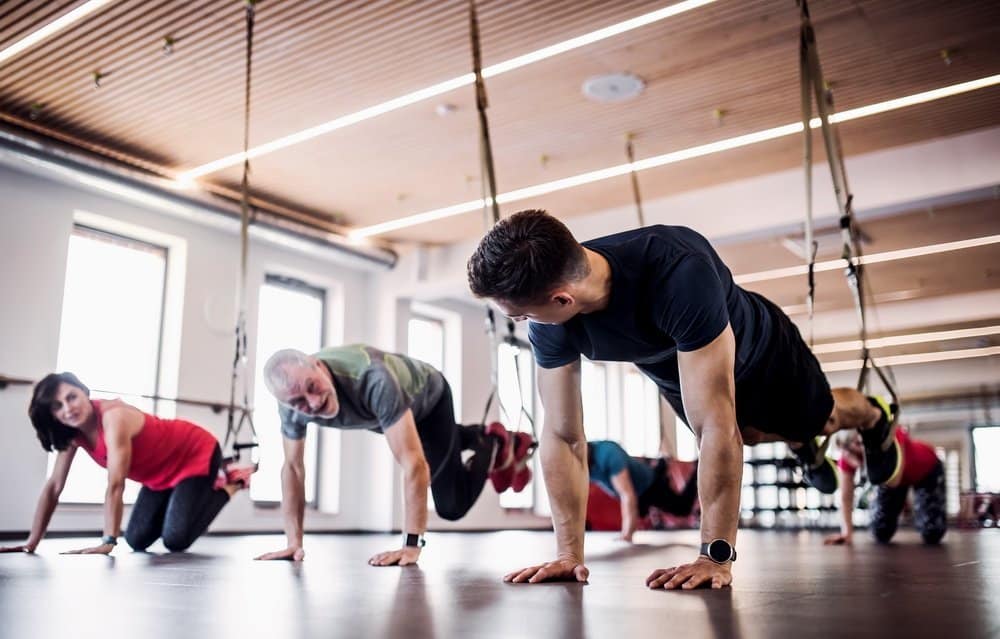 A group of cheerful seniors in gym with a young personal trainer doing exercise with TRX. - The Metabolic Reset Diet Plan