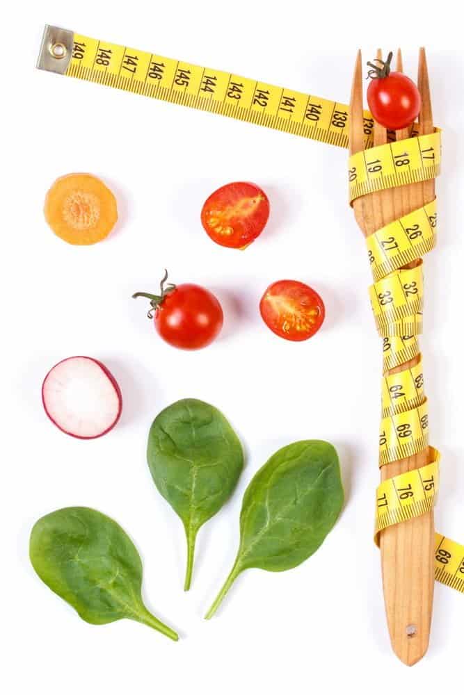 Tips on Lose Weight Quickly - Fork wrapped in centimeter and fresh vegetables, concept of lose weight and healthy nutrition Tips on Lose Weight Quickly - Wooden fork wrapped in tape measure and fresh ripe vegetables on white background, concept of lose weight and healthy nutrition