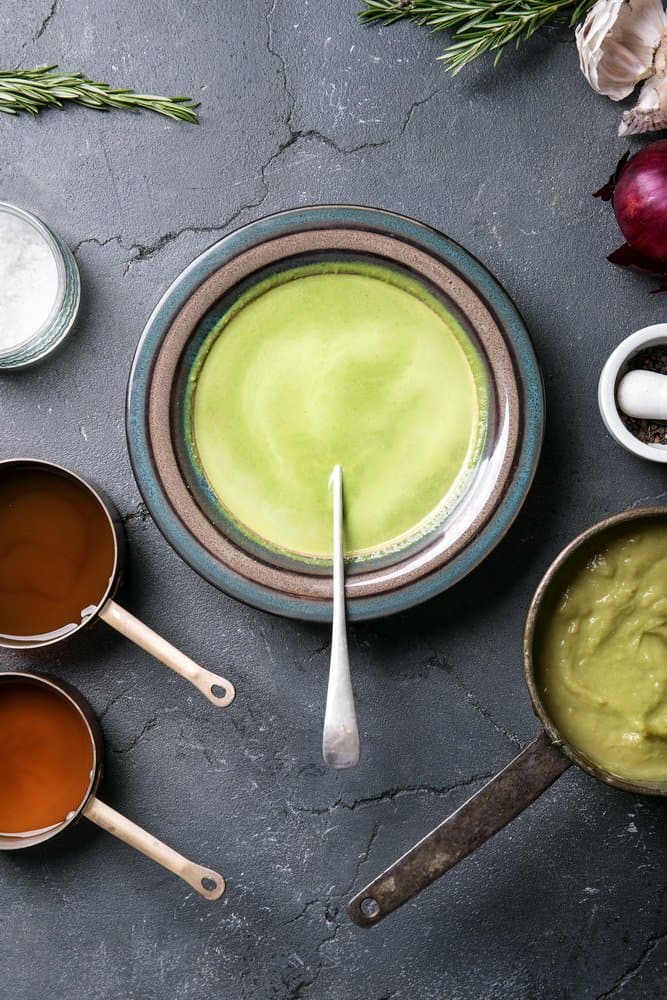 Home made broccoli and pea puree soup decorated with rosemary, thyme, garlic and onions, served with vegetable broth. Top View - The Metabolic Reset Diet Plan