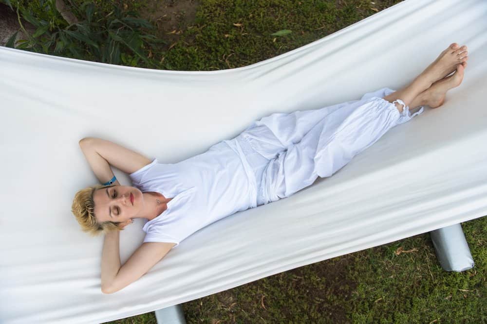 beautiful young woman enjoying free time while resting on white hammock in the backyard