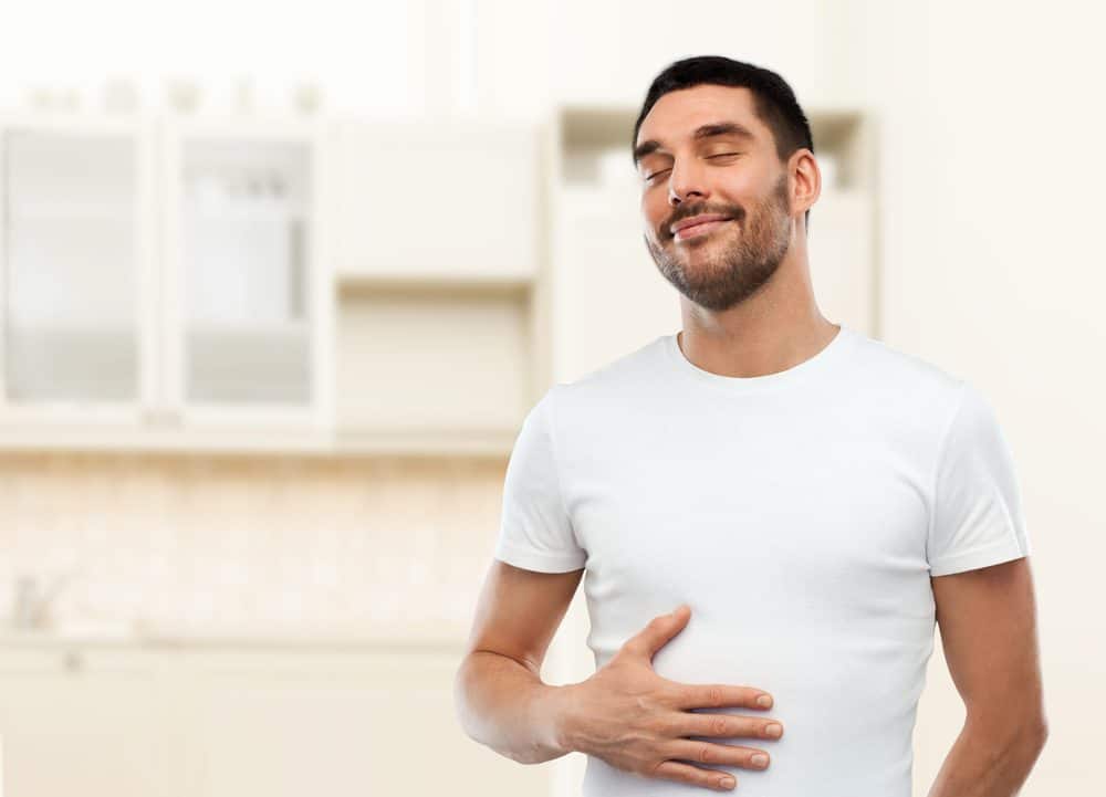Digestion, satisfaction and people concept - happy full man touching his tummy over kitchen background