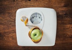Green apple wrapped in a tape measure on a white scale, wooden surface on background, dieting and weight loss concept - Top 10 Ways to Weight Loss
