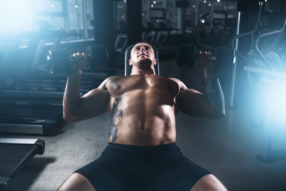 Muscular male bodybuilder training with dumbbells in sport gym. Bodybuilding workout. Power lifting - Amazing Facts About Fitness Muscular male bodybuilder training with dumbbells in sport gym. Bodybuilding workout. Power lifting - Amazing Facts About Fitness