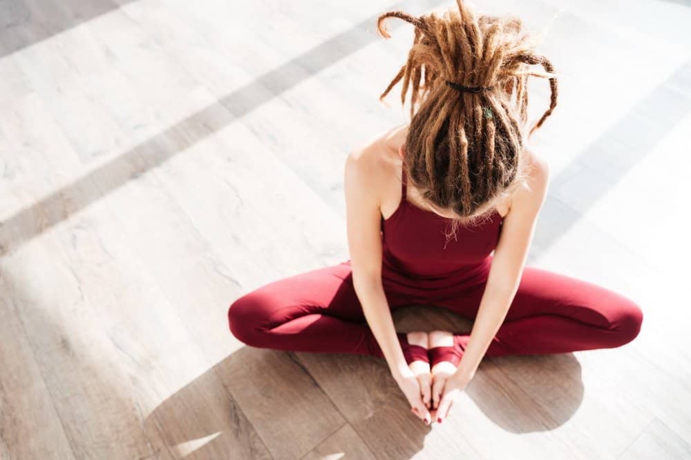 Top view of modern young woman with dreadlocks sitting and doing yoga on wooden floor - Amazing Facts About Fitness Top view of modern young woman with dreadlocks sitting and doing yoga on wooden floor - Amazing Facts About Fitness