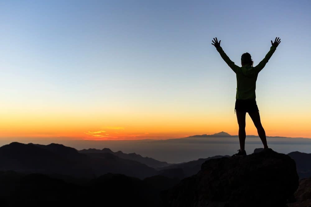 Woman successful hiking climbing silhouette in mountains, motivation and inspiration in beautiful sunset and ocean. Female hiker with arms up outstretched on mountain top looking at beautiful night sunset inspirational landscape. 
