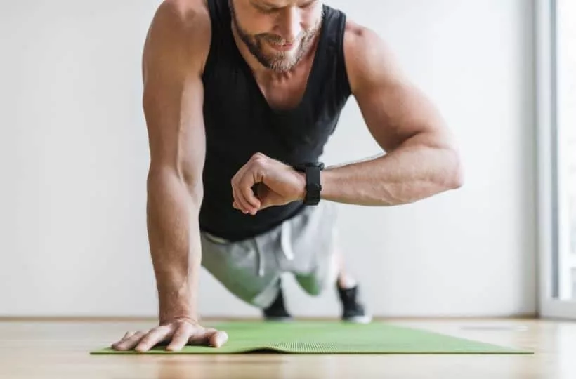 Man exercising at home on a yoga mat while checking his smartwatch