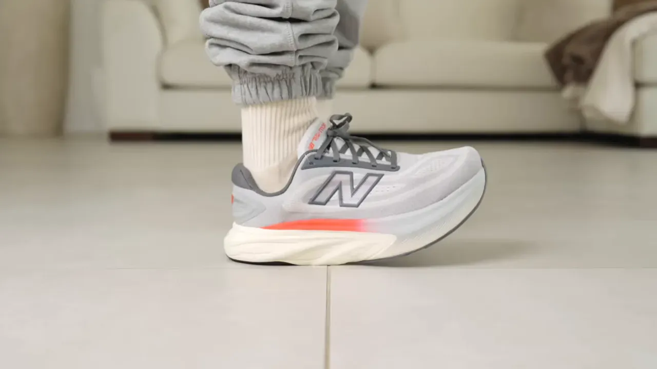 Person wearing gray New Balance running shoe with orange accent, standing on tile.