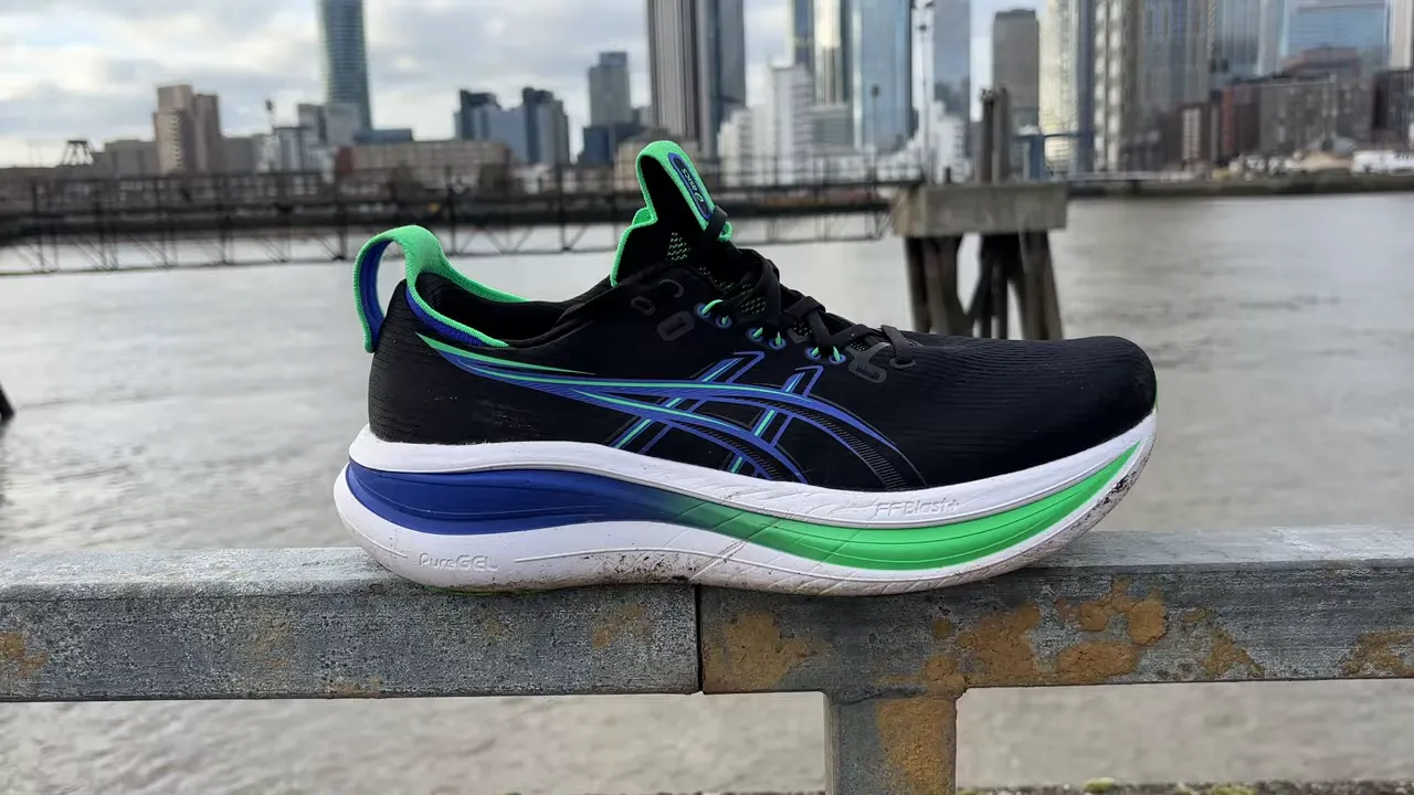 Asics Gel Nimbus 28 running shoe on a metal railing with a city skyline and river in the background.
