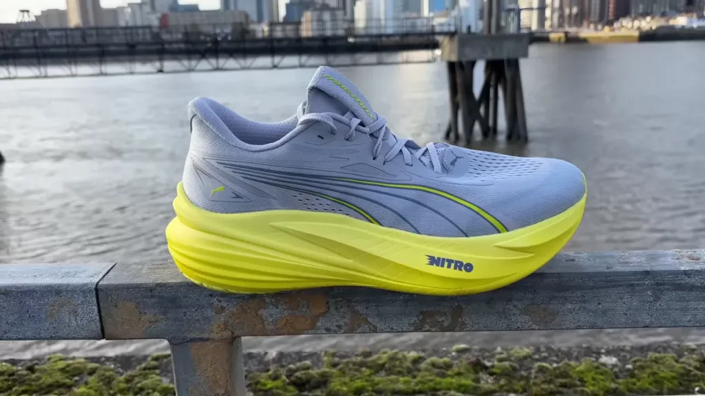 Puma MagMax 2 running shoe in gray and yellow on a railing with a city and river in the background.