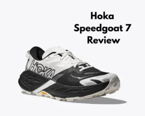 Close-up shot of a white and black Hoka Speedgoat 7 trail running shoe. The shoe features a Vibram Megagrip outsole and the Hoka logo. It is displayed on a text